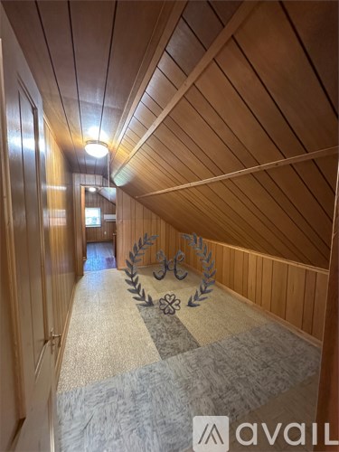 A long, narrow room with wooden walls and ceiling, carpeted floor, and a row of decorative plants on the wall.