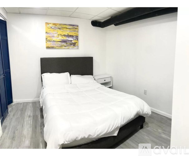 A bedroom with a white bed and a painting on the wall.
