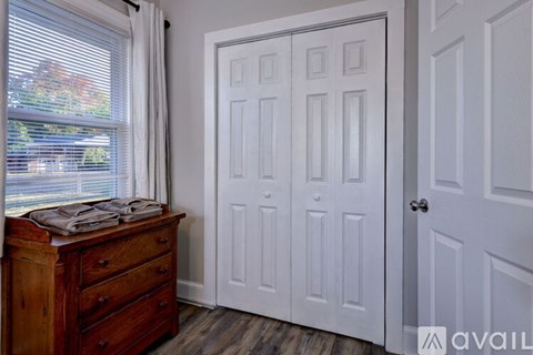 A white door is in a room with a wooden dresser and a window.