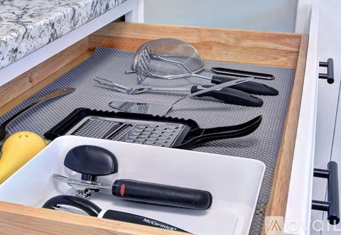 A kitchen drawer with a variety of utensils and a yellow squash.