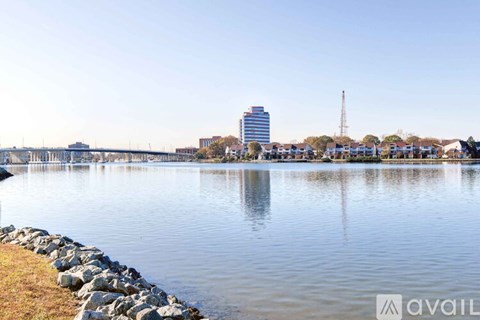 A calm lake with a cityscape in the background and a stone wall in the foreground.