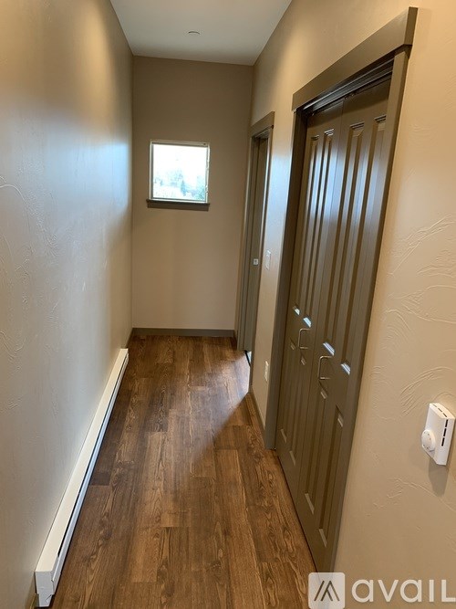 A hallway with wooden floors and a white wall with a window.