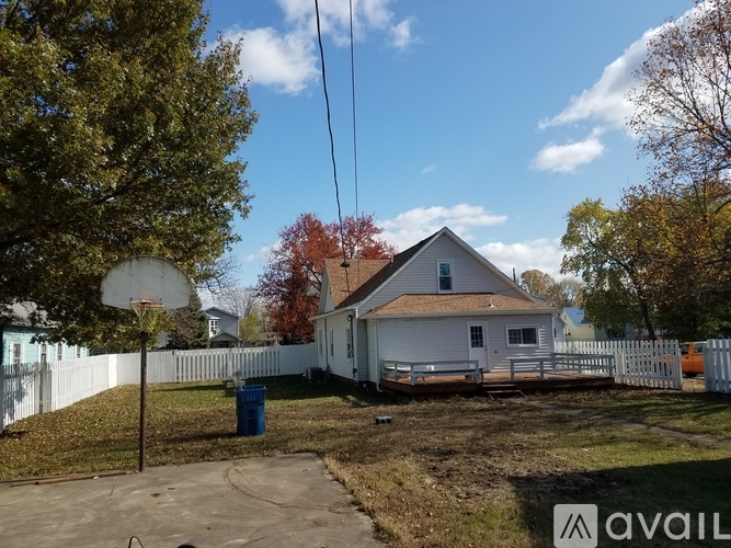A house with a white picket fence and a blue trash can in front.
