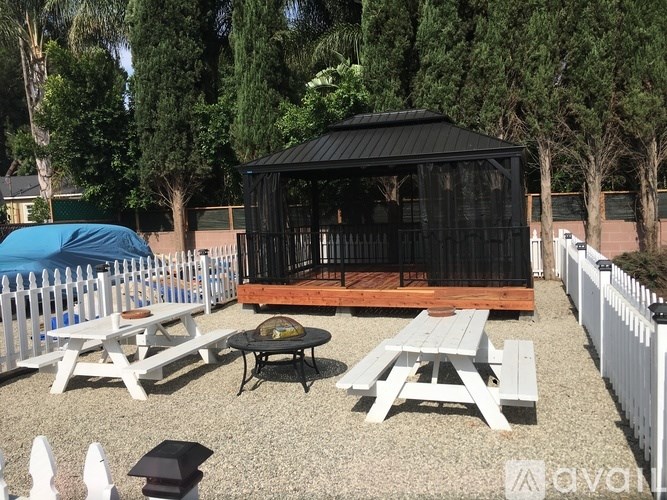 A black gazebo is surrounded by picnic tables and benches.