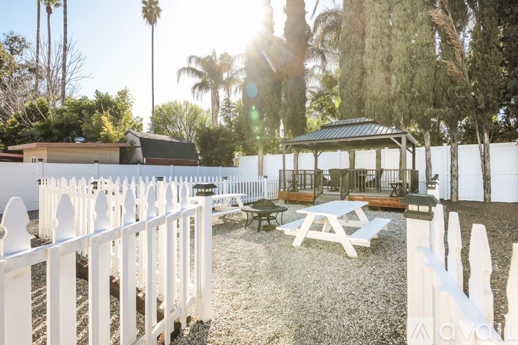 A white picket fence surrounds a picnic area with a gazebo.