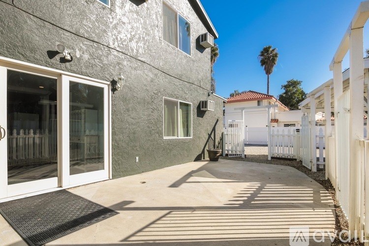A grey house with a white fence and a palm tree in the background.