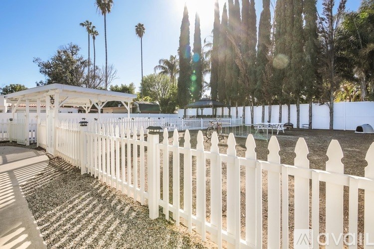 A white picket fence in front of a house with a tree in the background.