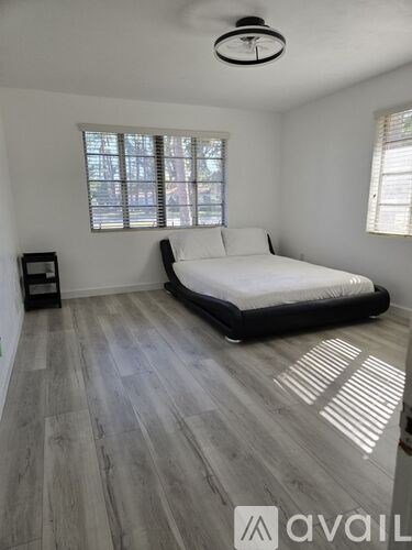 A bedroom with a bed, a window with blinds, and a wooden floor.
