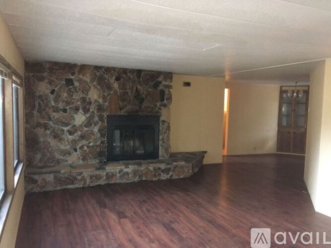 A stone fireplace in a room with wooden floors and a door in the background.
