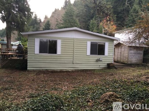 A small house with a green siding is surrounded by trees.