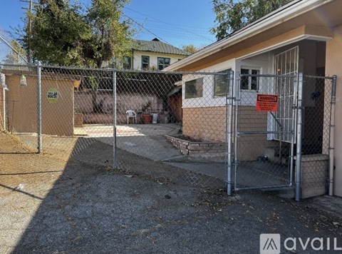 A chain link fence surrounds a small building with a gate that has a red sign on it.
