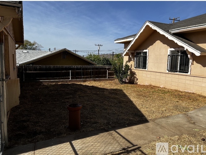 A backyard with a fence, a trash can, and a house.