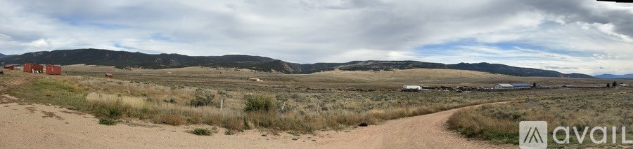 A dirt road leads through a grassy field with mountains in the distance.
