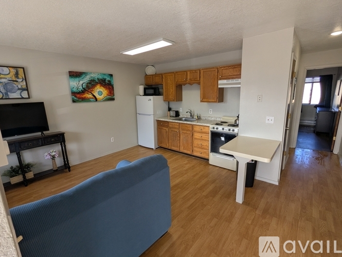 A living room with a blue couch and a kitchen area with a white refrigerator and wooden cabinets.