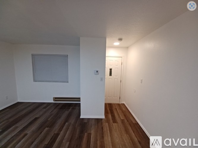A room with wooden floors and white walls, with a window and a door visible.