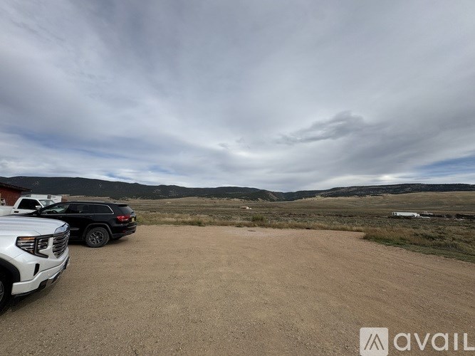 Two cars are parked in a dirt lot with a cloudy sky above.
