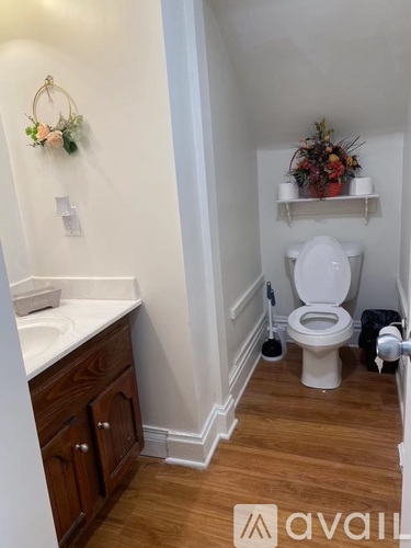 A white toilet in a small bathroom with wooden floors and white walls.