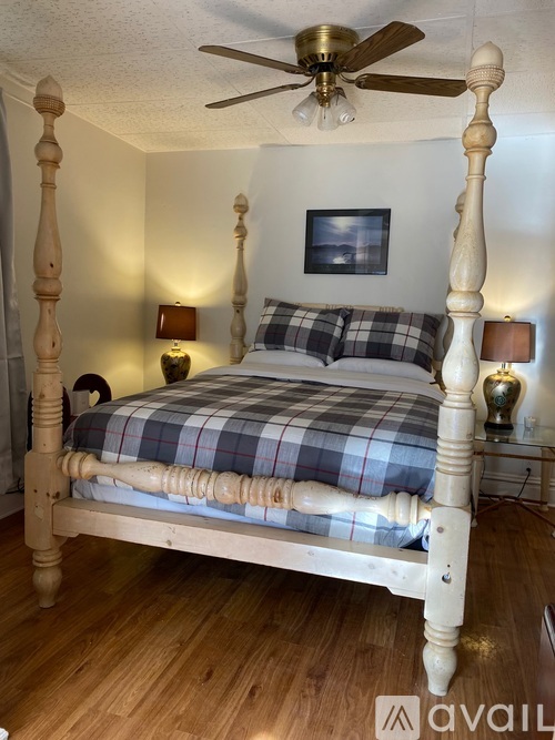 A bedroom with a bed, pillows, a ceiling fan, and a picture on the wall.