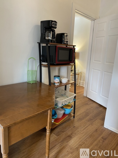 A wooden table with a shelf on top of it holding a microwave, a toaster, and a coffee maker.