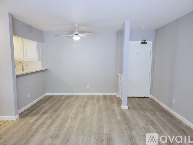 A room with a ceiling fan and light, wooden flooring, and a white door.
