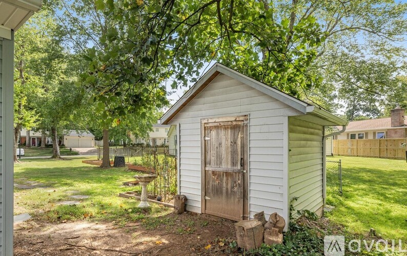A small white shed with a wooden door sits in a grassy area.