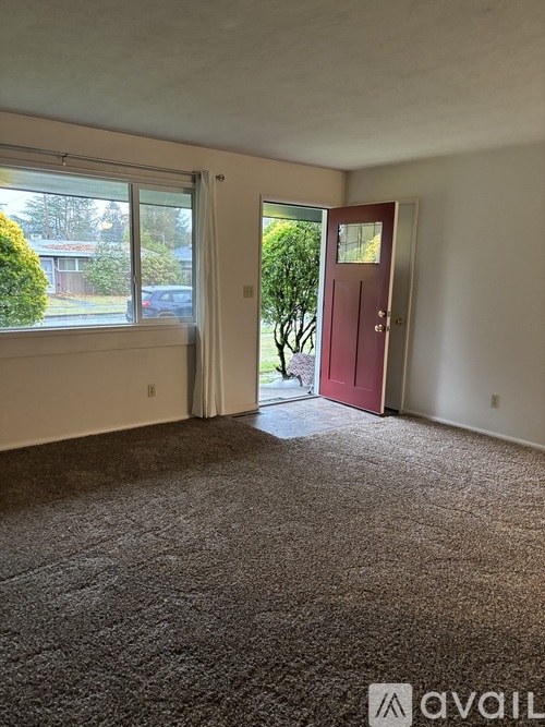 A room with a carpeted floor, a red door, and a window with blinds.