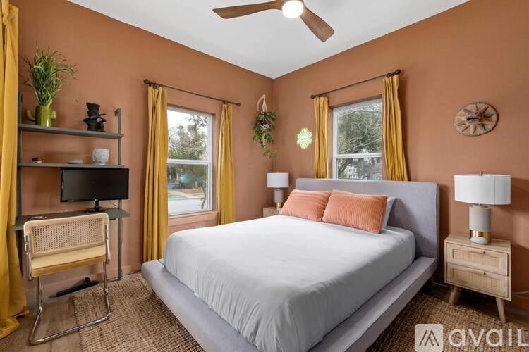 A bedroom with a bed, a chair, a ceiling fan, and a window with yellow curtains.
