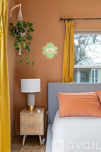 A bedroom with a bed, a nightstand with a lamp, a hanging plant, and a wall decoration.