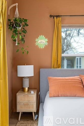 A bedroom with a bed, a nightstand with a lamp, a hanging plant, and a wall decoration.