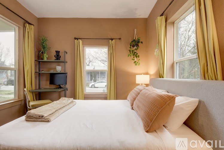 A bedroom with a large bed, a chair, and a window with yellow curtains.