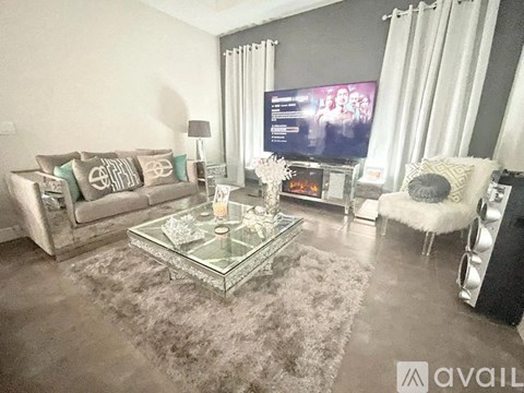 A living room with a grey couch, a glass coffee table, and a television on the wall.