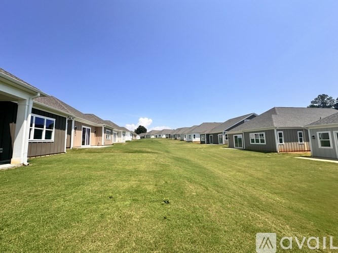A row of houses with a grassy field in the foreground and a clear blue sky above.