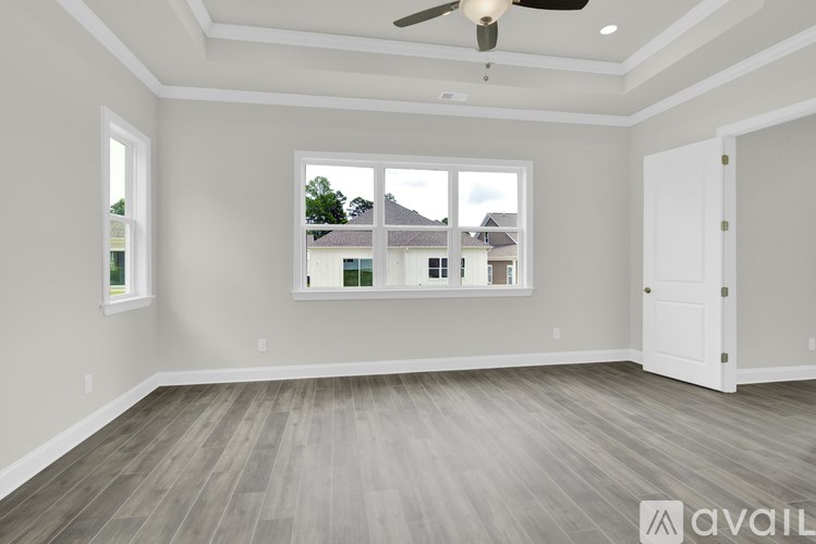 A spacious room with a ceiling fan and a view of houses across the street through the window.