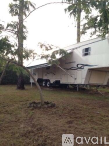 A white trailer with a black design on the side is parked in a grassy area.