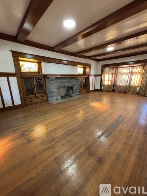 A spacious room with wooden floors and a stone fireplace.