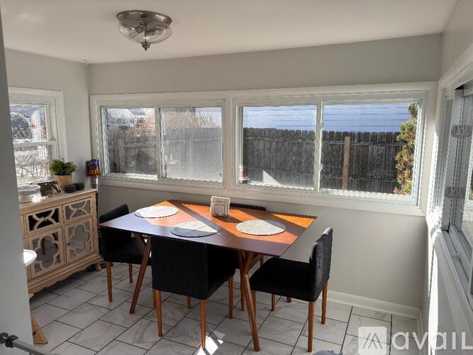 A dining room with a table set for two and a view of a fence outside the window.