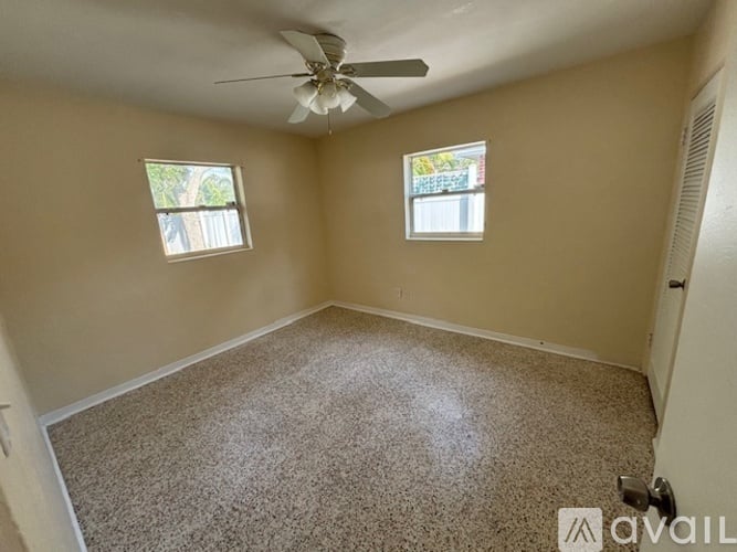 A room with a carpeted floor, a ceiling fan, and two windows.