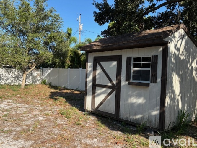 A small white shed with a brown roof and a black door is situated in a grassy area.