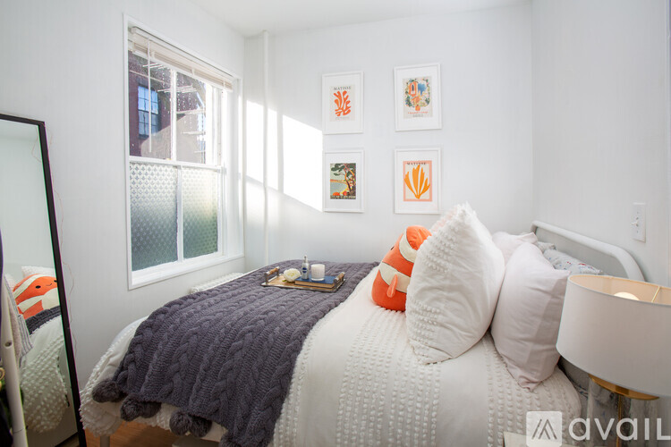 A bedroom with a bed, pillows, a blanket, a lamp, a mirror, and pictures on the wall.
