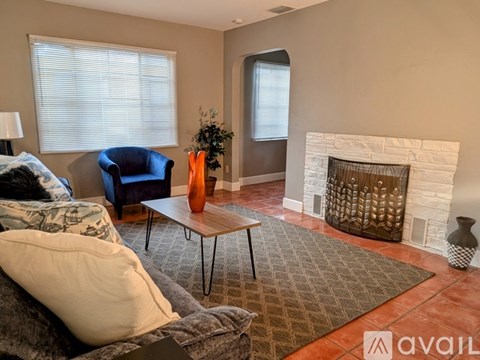 A living room with a grey couch, a white fireplace, and a brown rug.