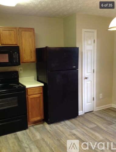 A black refrigerator stands in a kitchen with wooden cabinets and a black oven.