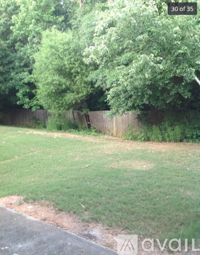 A grassy area with a fence and trees in the background.