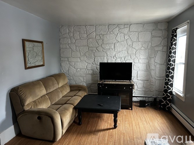 A living room with a tan couch, a black coffee table, and a stone wall.