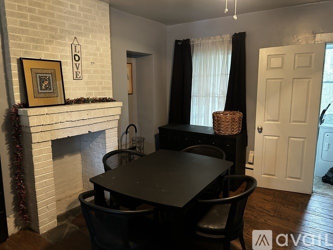 A black dining table with four chairs is set in a room with a white brick fireplace.
