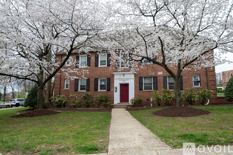 A brick building with a red door and windows with trees in front.