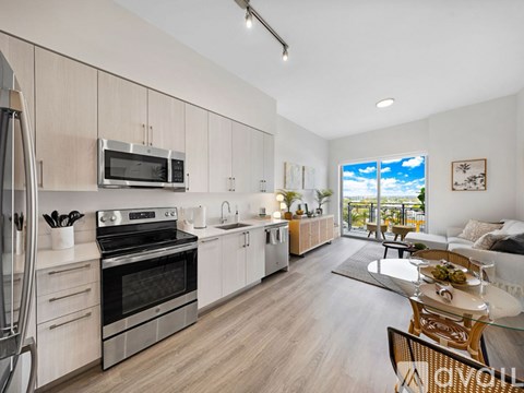 A modern kitchen with a stainless steel oven and microwave, wooden cabinets, and a dining area with a glass table.
