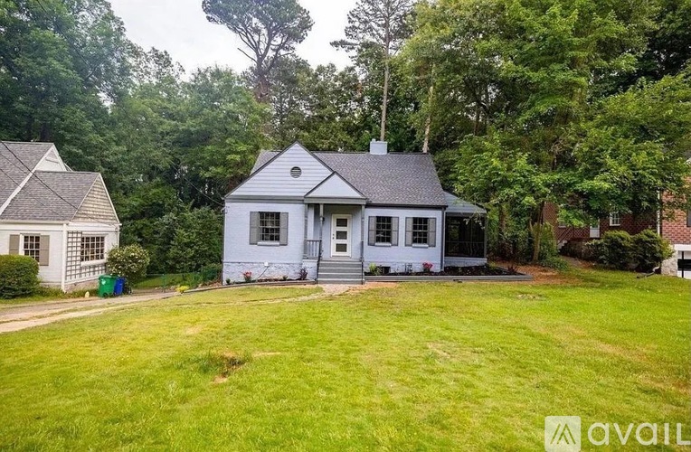 A house with a white exterior and a grey roof is surrounded by greenery.