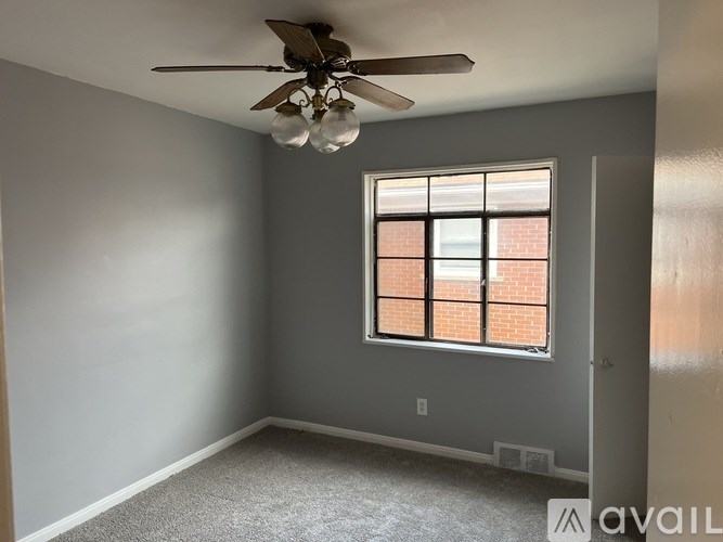 A room with a ceiling fan and a window with a brick wall outside.