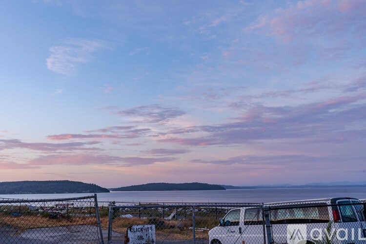 A white van is parked by a fence with a sign that says "Parking Available".