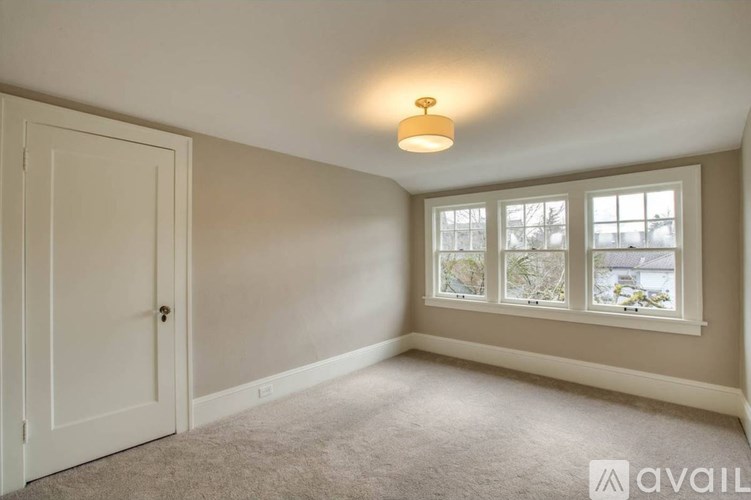 A room with a carpeted floor, a door, and a window with a view of trees and a building outside.